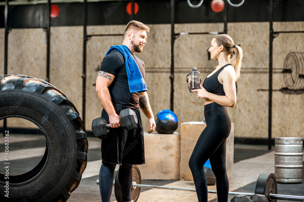 Young athletic couple talking together in the crossfit gym during the break after the training