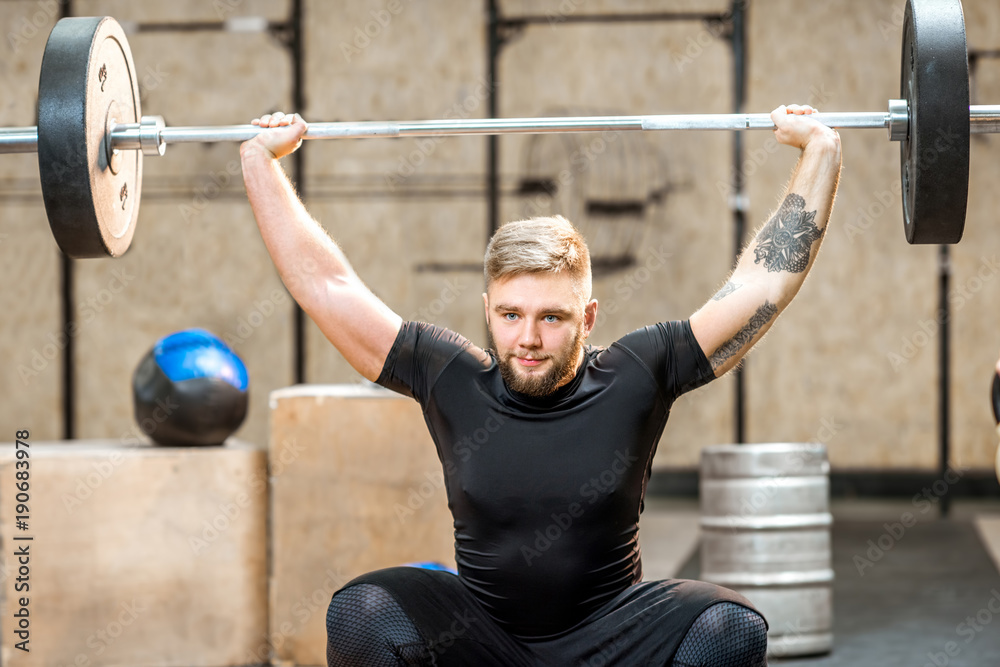 一名身穿黑色运动服的年轻运动男子在crossfit健身房举起打嗝