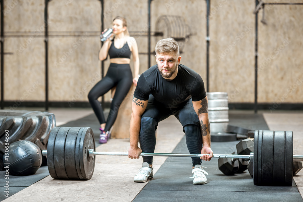 Handsome athletic man in black sports wear lifting up a heavy burbell in the crossfit gym