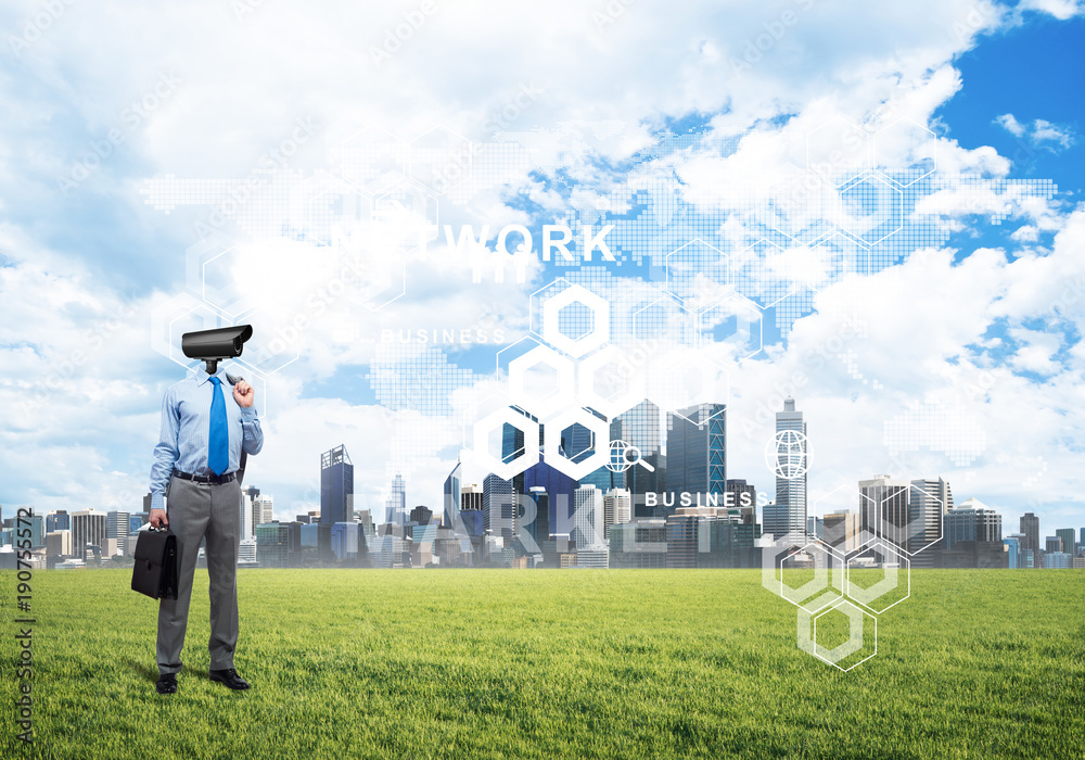 Camera headed man standing on green grass against modern cityscape