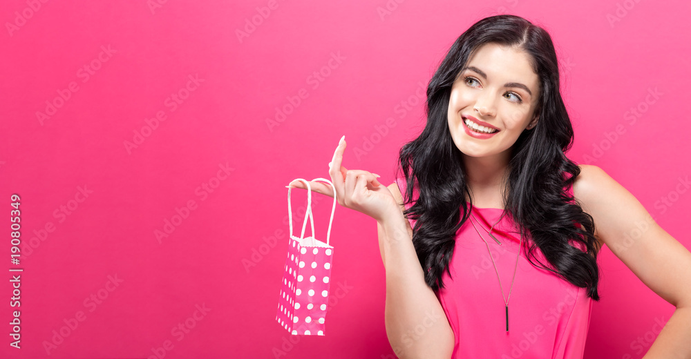 Young woman holding a tiny shopping bag on a pink background