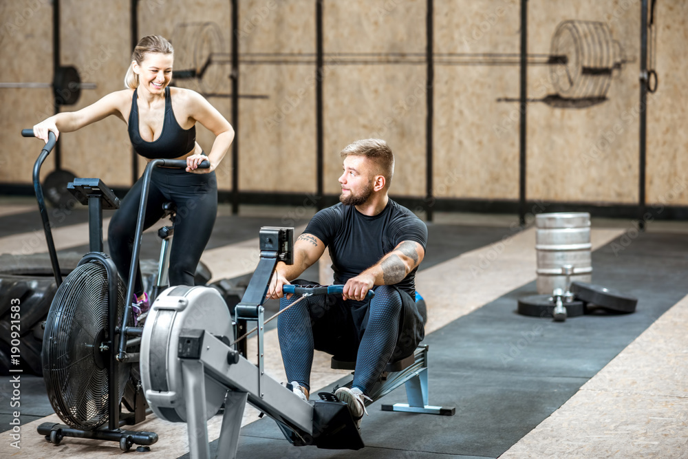 Young couple training on the exercise air bicycle and rowing machine in the gym