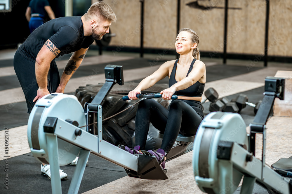 Handsome coach training woman on the exercise rowing machine in the gym