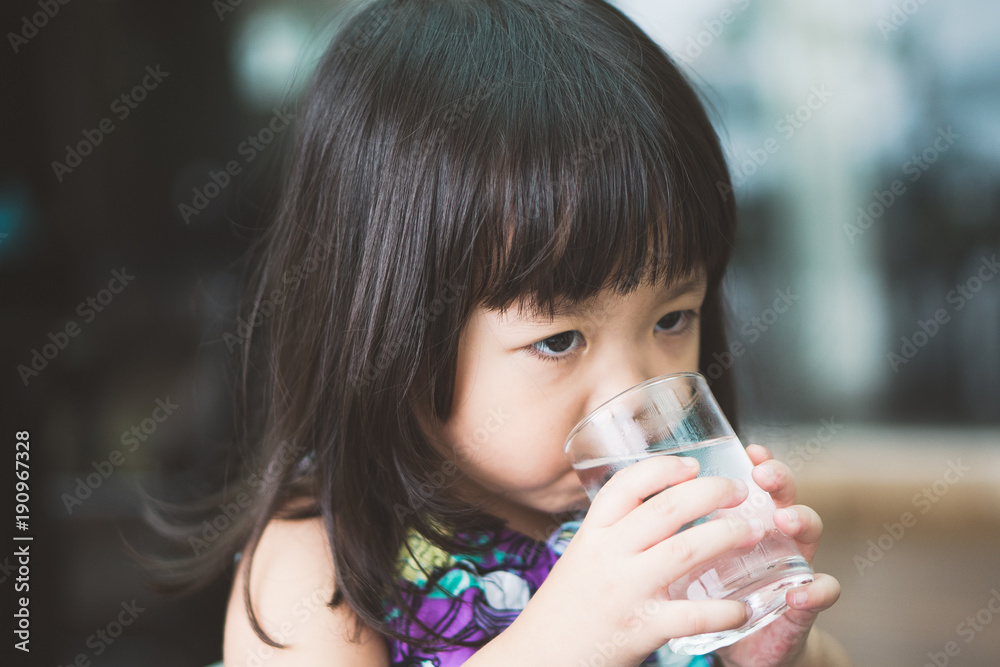 Happy adorable little girl drinking water.Smiling asian kid holding transparent glass in her hand.