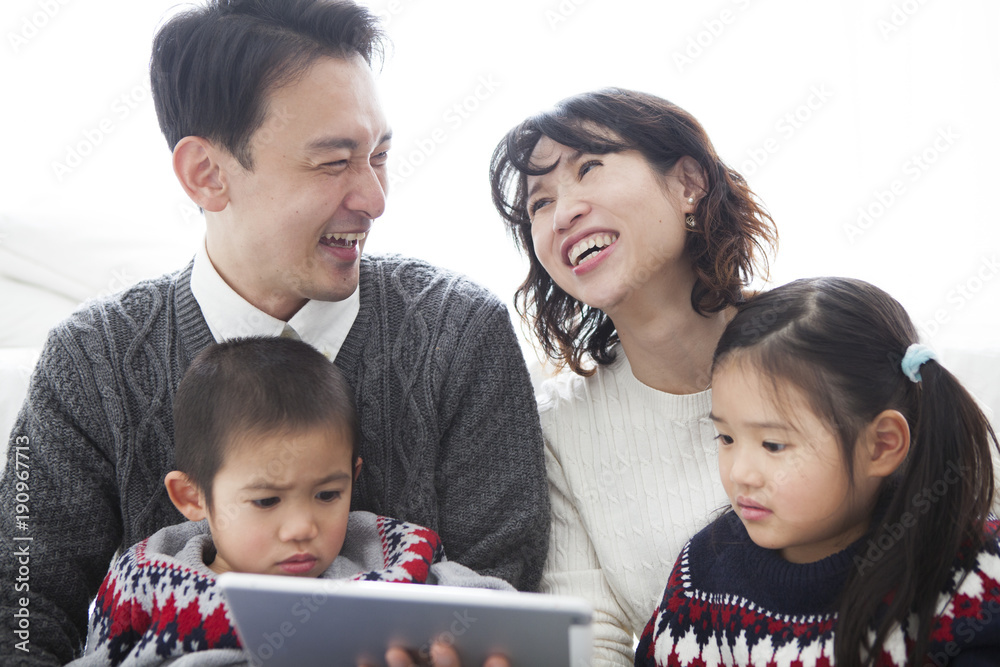 お父さんとお母さんが笑顔で話している。タブレットを見ている娘と息子。