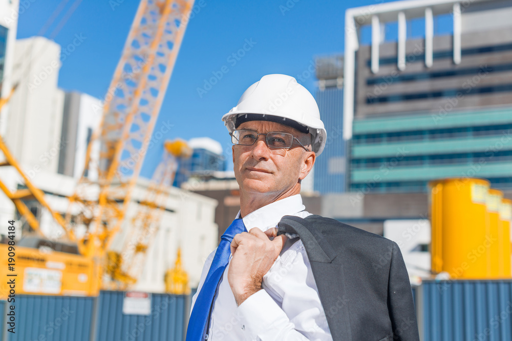 Senior elegant builder man in suit at construction site on sunny summer day