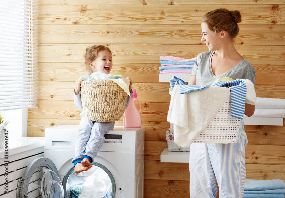 Happy family mother housewife and child   in laundry with washing machine