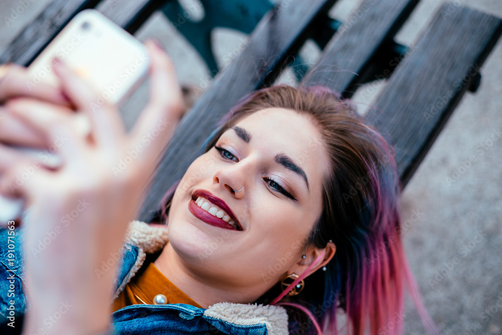 Portrait of a hipster girl lying on a bench using phone.