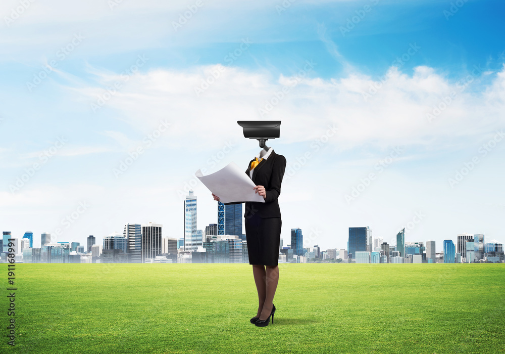 Camera headed woman standing on green grass against modern cityscape