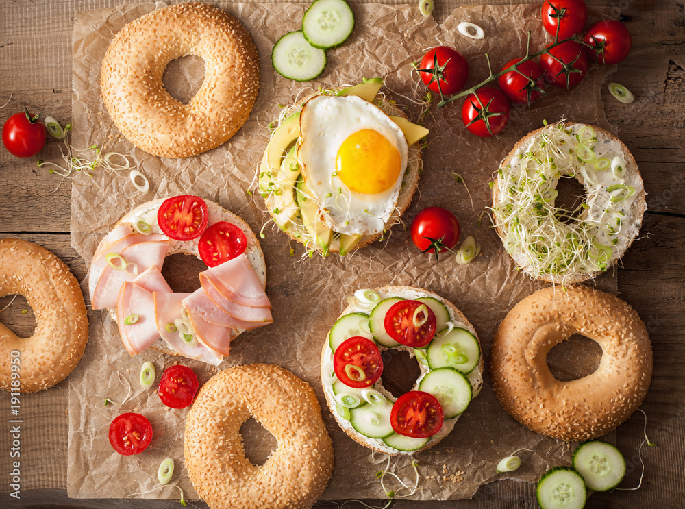 variety of sandwiches on bagels: egg, avocado, ham, tomato, soft cheese, alfalfa sprouts