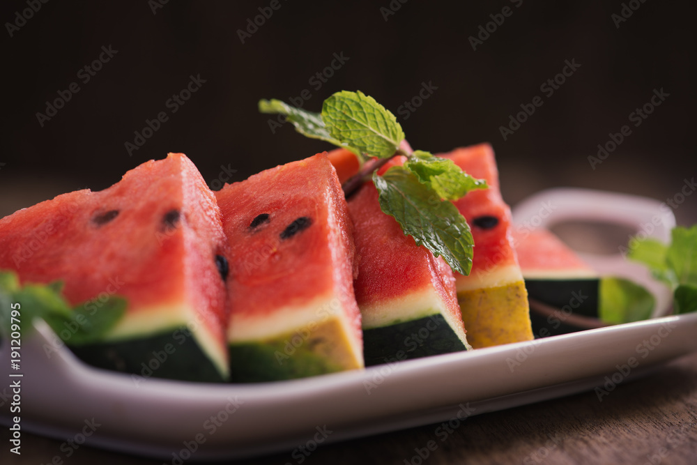 Fresh sliced watermelon in white dish on wooden table.