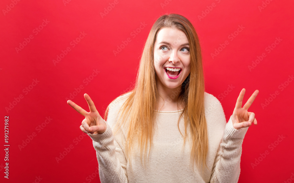 Young woman giving the peace sign on a solid background