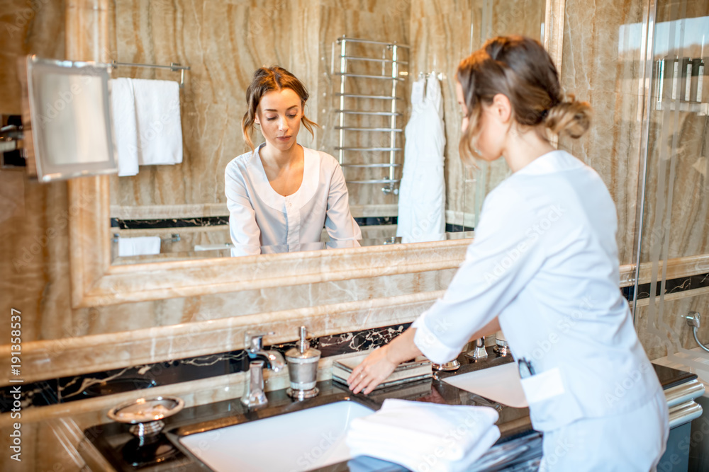 Young chambermaid in uniform cleaning a bathroom in the hotel