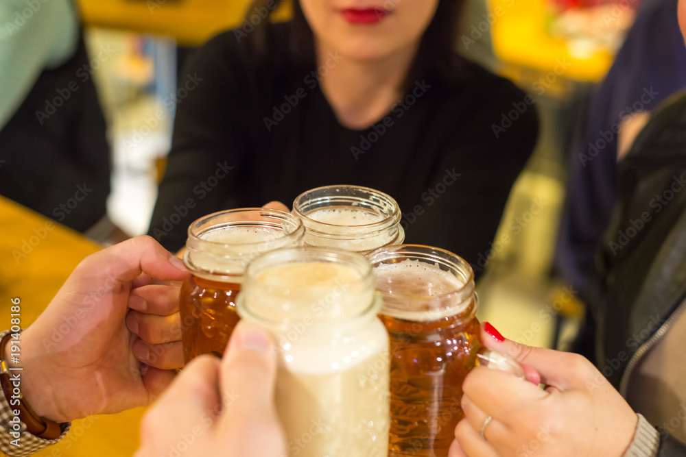 朋友们在酒吧餐厅用自制啤酒欢呼——年轻人双手敬酒，啤酒半便士