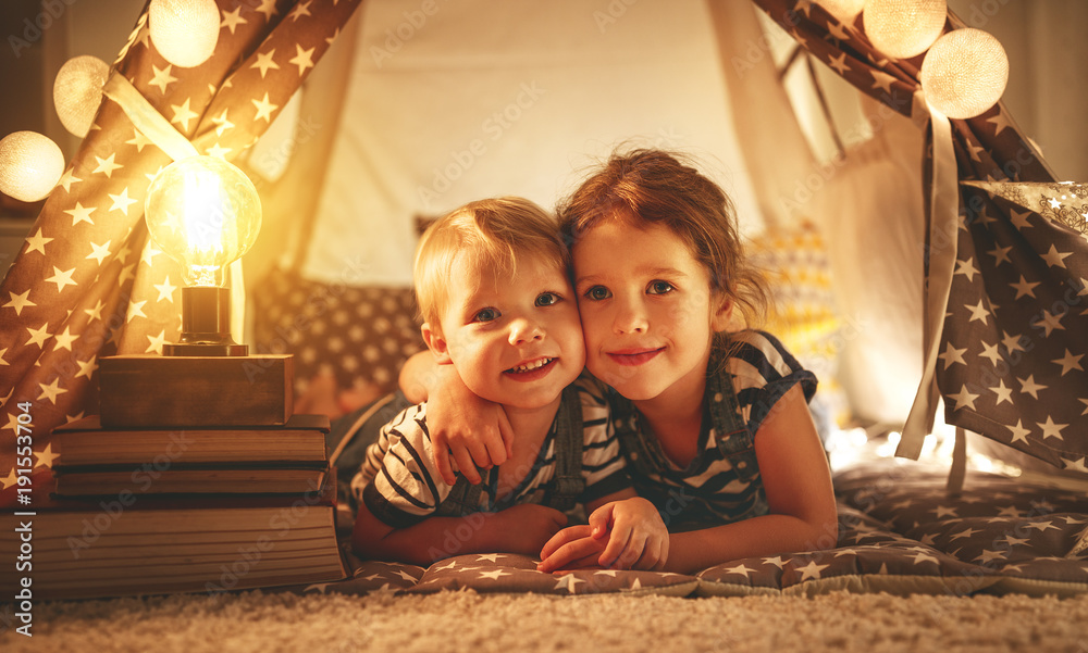 happy family children brother and sister play, laugh and hug   in dark tent in playroom