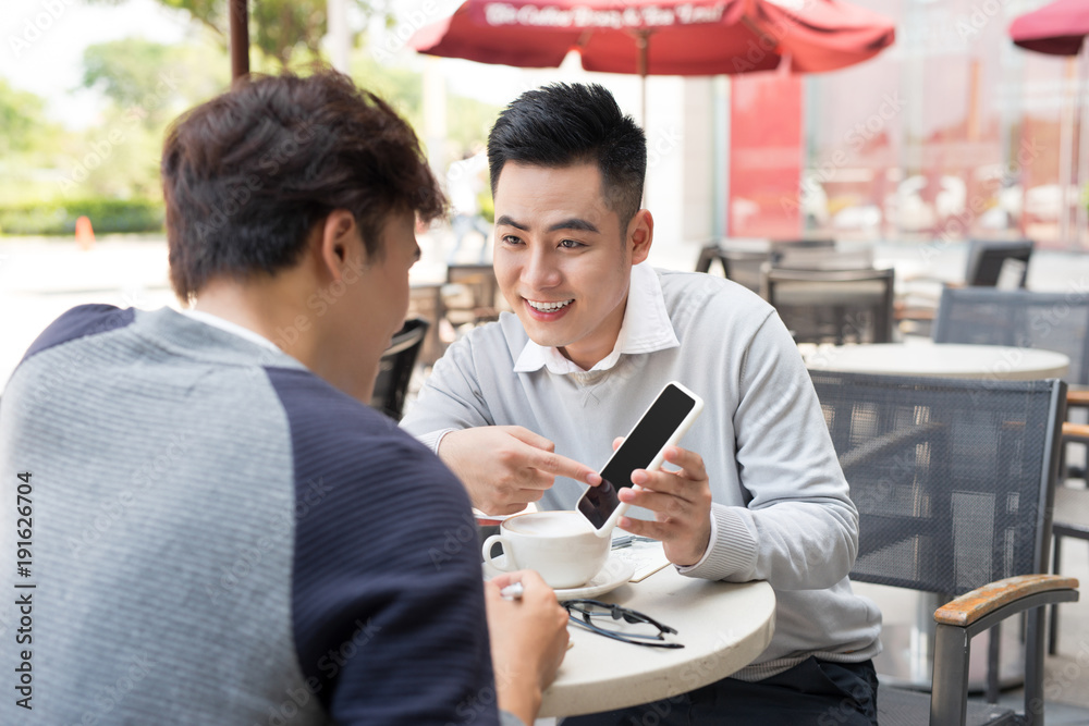 Asian young men enjoying watching on mobile phone together in cafe with coffee on the table.