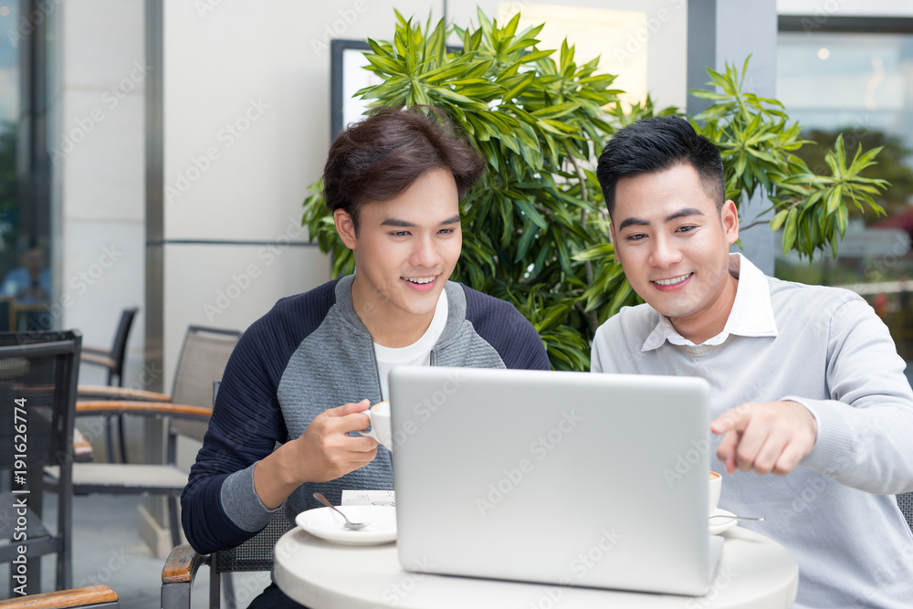 Two attractive mature students talking and working outdoors on laptop