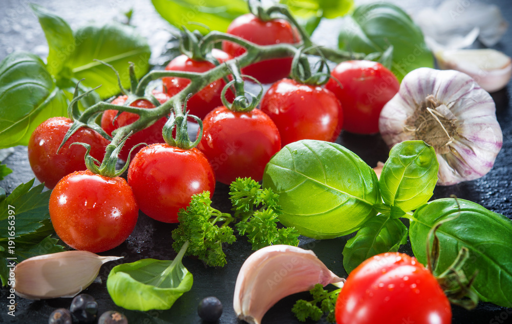 Ripe tomatoes with fresh basil, garlic and other herbs with water drops on slate plate