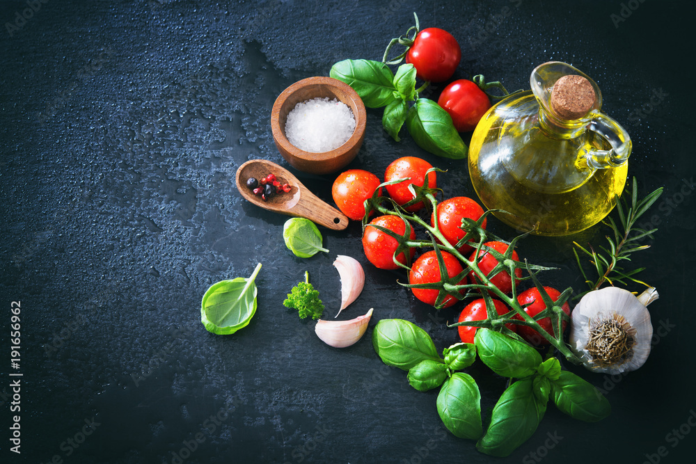 Olive oil, tomatoes, garlic, parsley, basil, spices on dark background with water drops