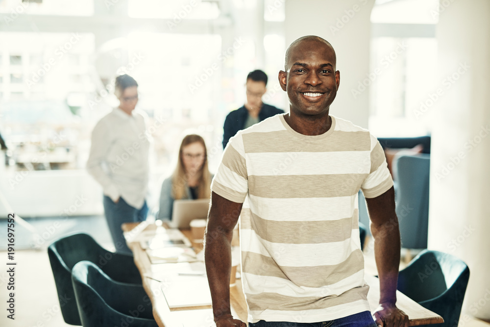 Young African designer smiling with colleagues working in the background