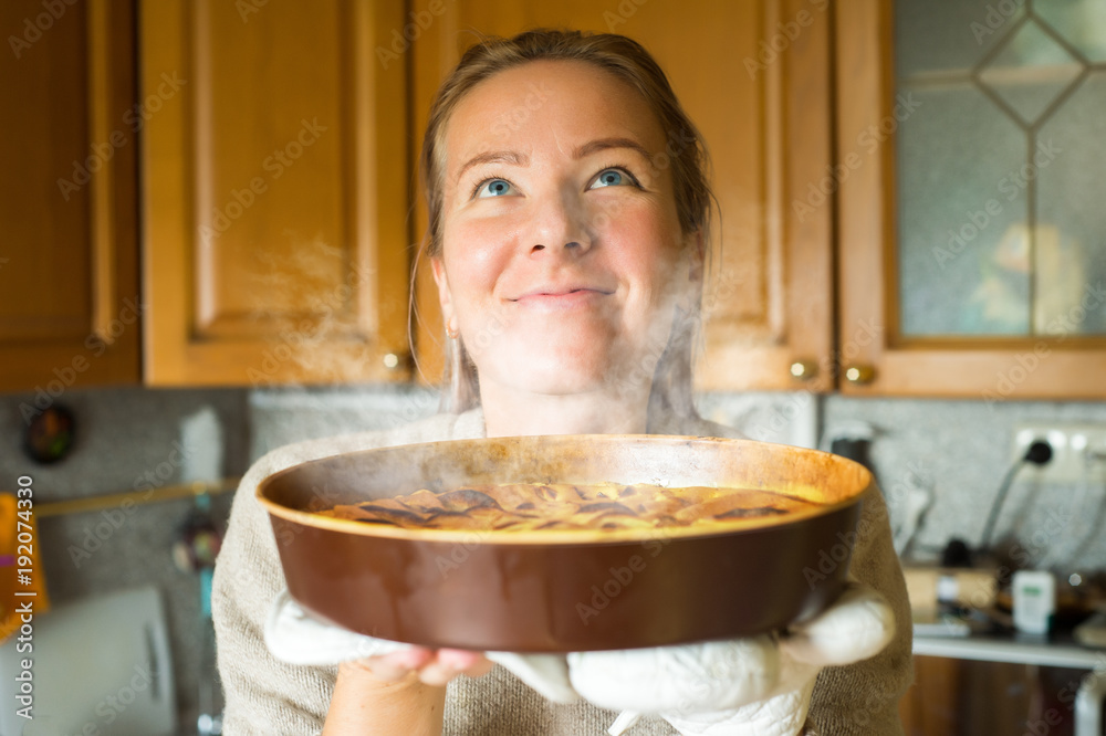 Young woman holding a baking tray with a ready cake