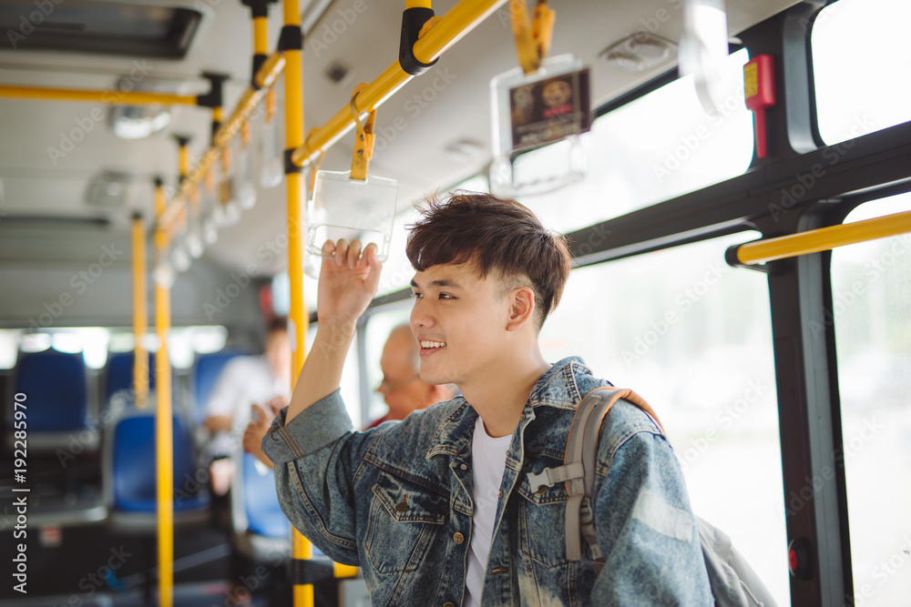 Asian man taking public transport, standing inside bus.