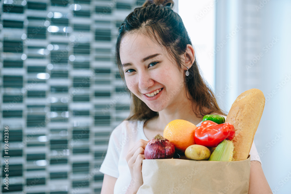 在她甜蜜的家里，一位亚洲妇女把水果装在纸袋里放在厨房里做晚饭。