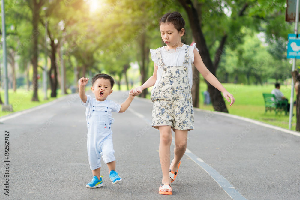 亚洲姐妹牵着走在公园里阳光明媚的路上的小孩。