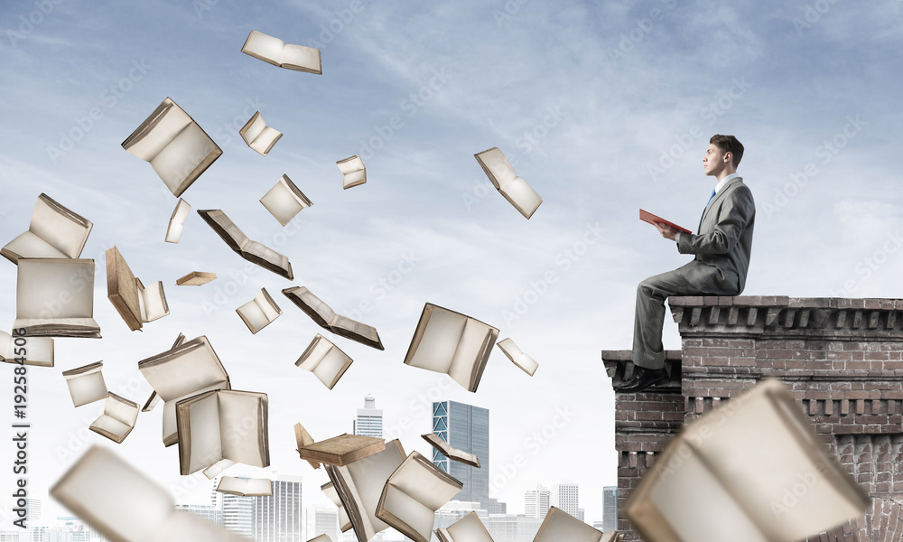 Man on roof reading book and many of them flying in air