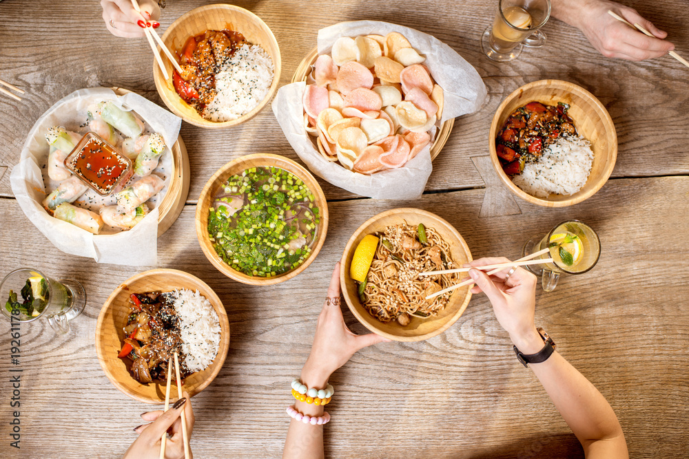 餐桌上的俯视图，桌上摆满了装在木板里的不同亚洲饭菜，年轻人在吃