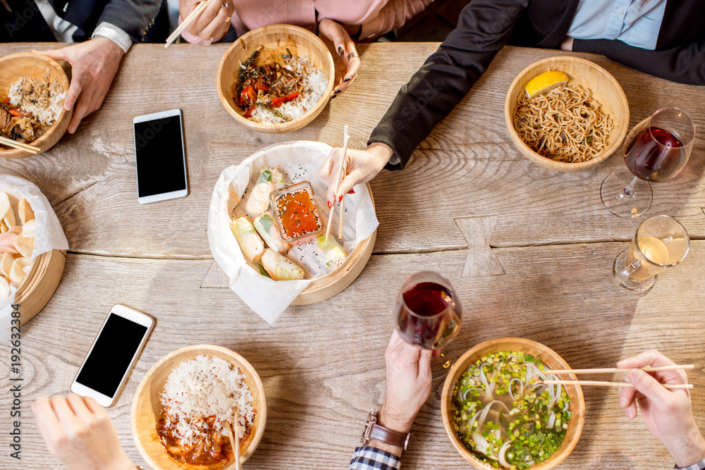 餐桌上的俯视图，桌上摆满了装在木板里的不同亚洲饭菜，人们在吃wi