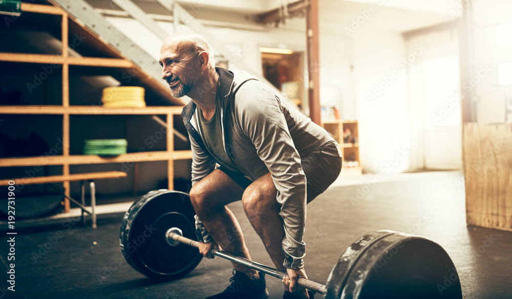 Fit mature man lifting heavy weights during a workout session