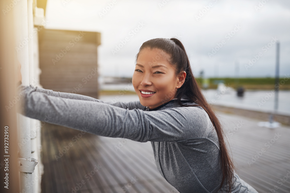 Smiling young Asian woman stretching outdoors before exercising