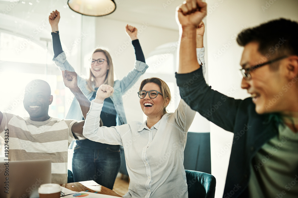 Diverse group of ecstatic colleagues cheering together in an office