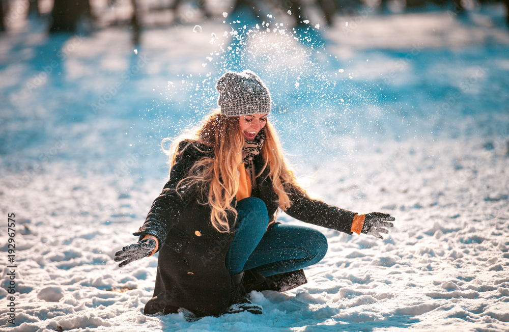 微笑的女人在阳光明媚的冬日向空中扔雪