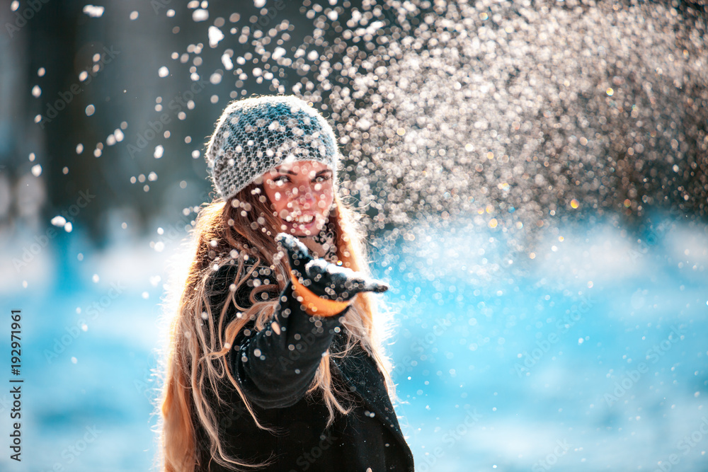 Smiling young woman throwing snow in the air looking at camera