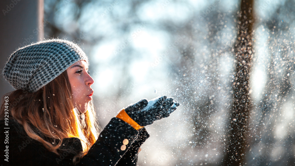 冬日女人在阳光明媚的日子里在户外吹雪，雪花纷飞