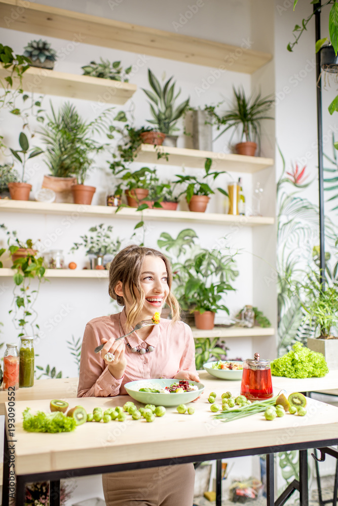 年轻女子拿着健康食品坐在美丽的室内，背景是绿色的花朵