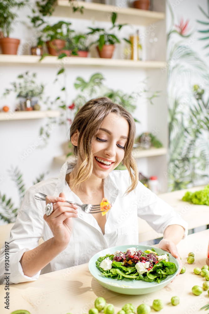 Young woman eating healthy food sitting in the beautiful interior with green flowers on the backgrou