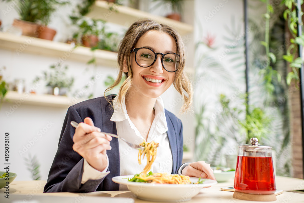 女商人在绿色背景下的素食餐厅享用意大利面和水果茶午餐