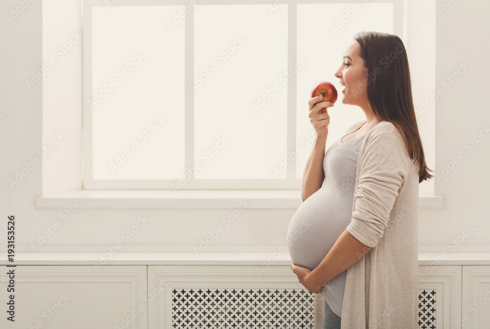 Pregnant woman eating apple at home copy space