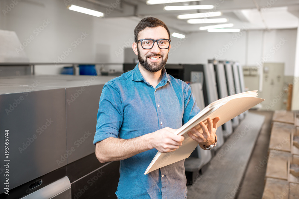 Portrait of a handsome typographer standing with stack of paper at the printing manufacturing with o