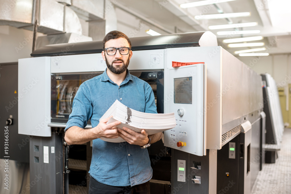 Portrait of a handsome typographer standing with stack of paper at the printing manufacturing with o