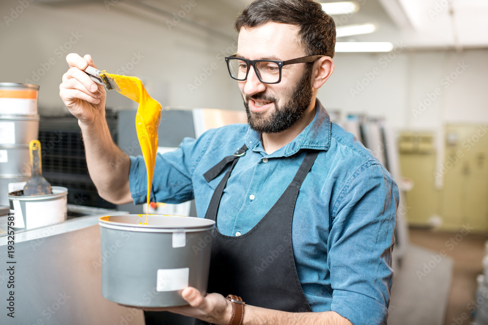 Typographer stiring yellow paint for offset machine standing at the printing manufacturing