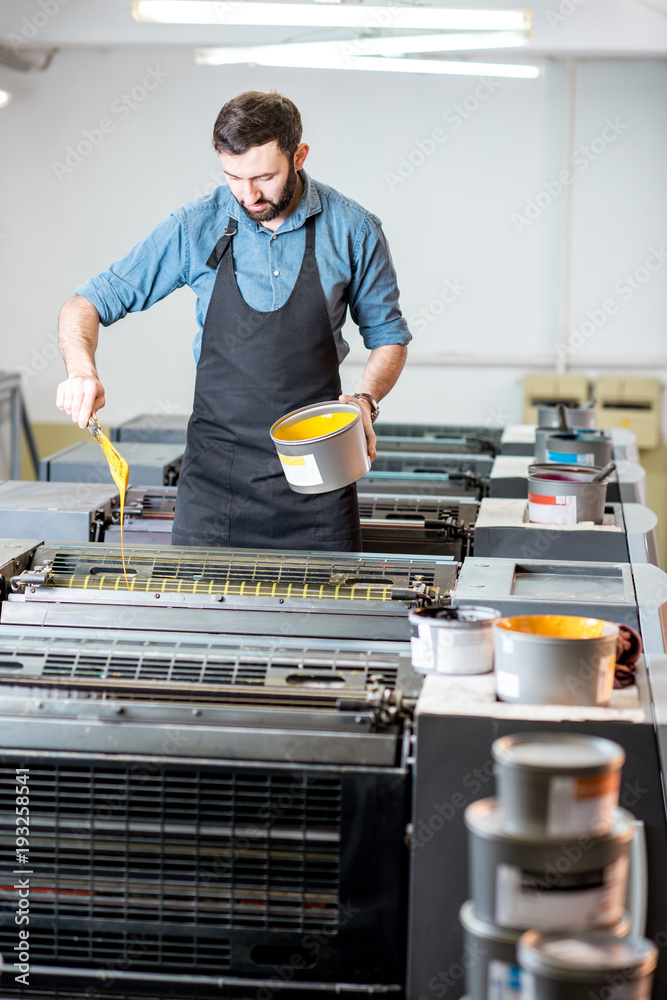 Typographer filling yellow paint into the offset machine at the printing manufacturing