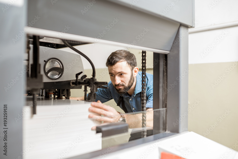 Man working with paper sheets feeling into the printing machine at the manufacturing