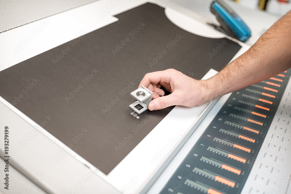 Checking the quality of the printing with magnifying glass on the operating desk of the printing man