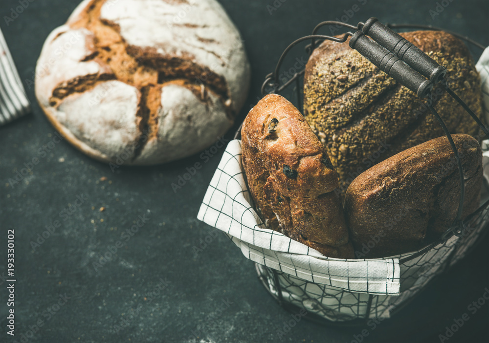 Various bread selection. Rye, wheat and multigrain rustic bread loaves on kitchen towels over black 