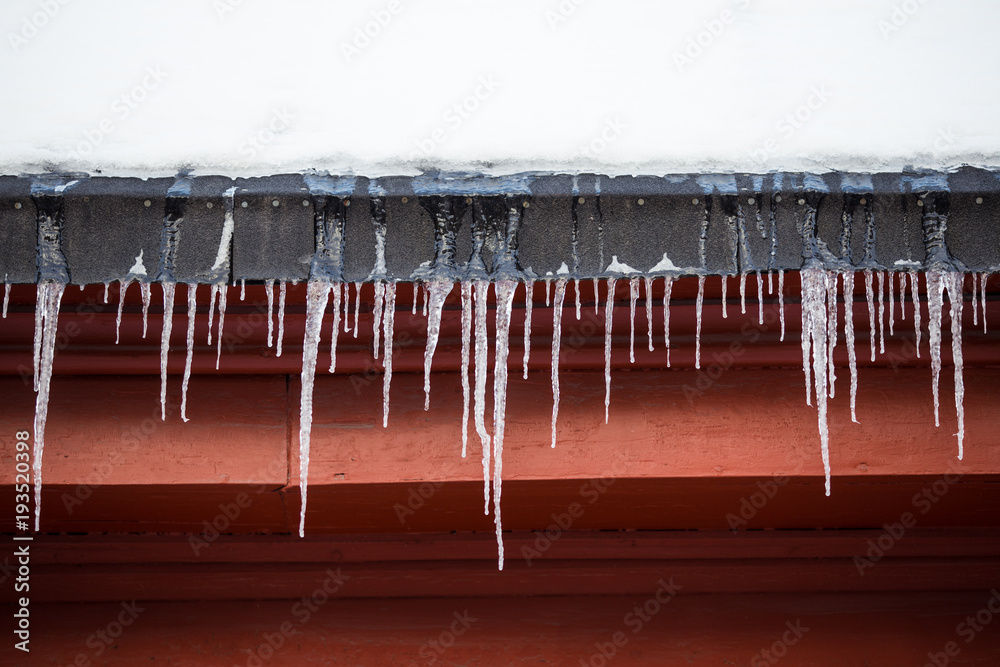 红色木质建筑被雪覆盖的屋顶上悬挂的冰柱细节