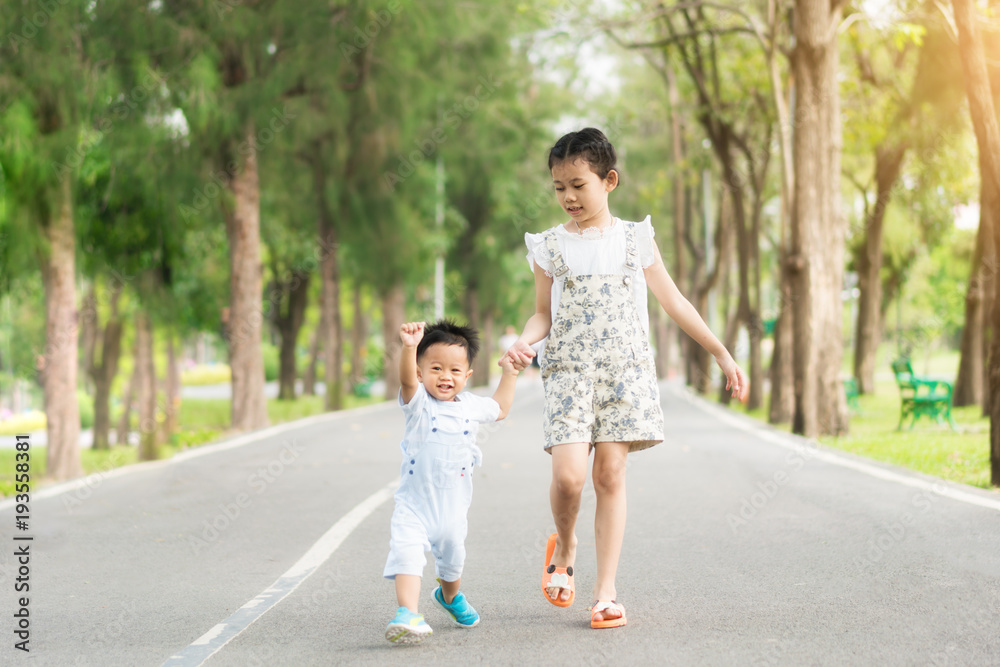 亚洲姐妹牵着走在公园里阳光明媚的路上的小孩。